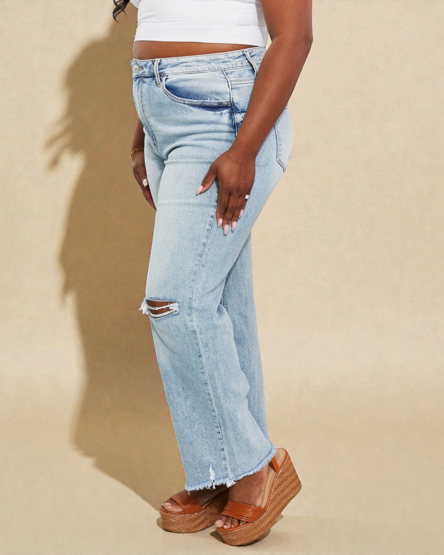 Person wearing light blue distressed jeans on a beige background