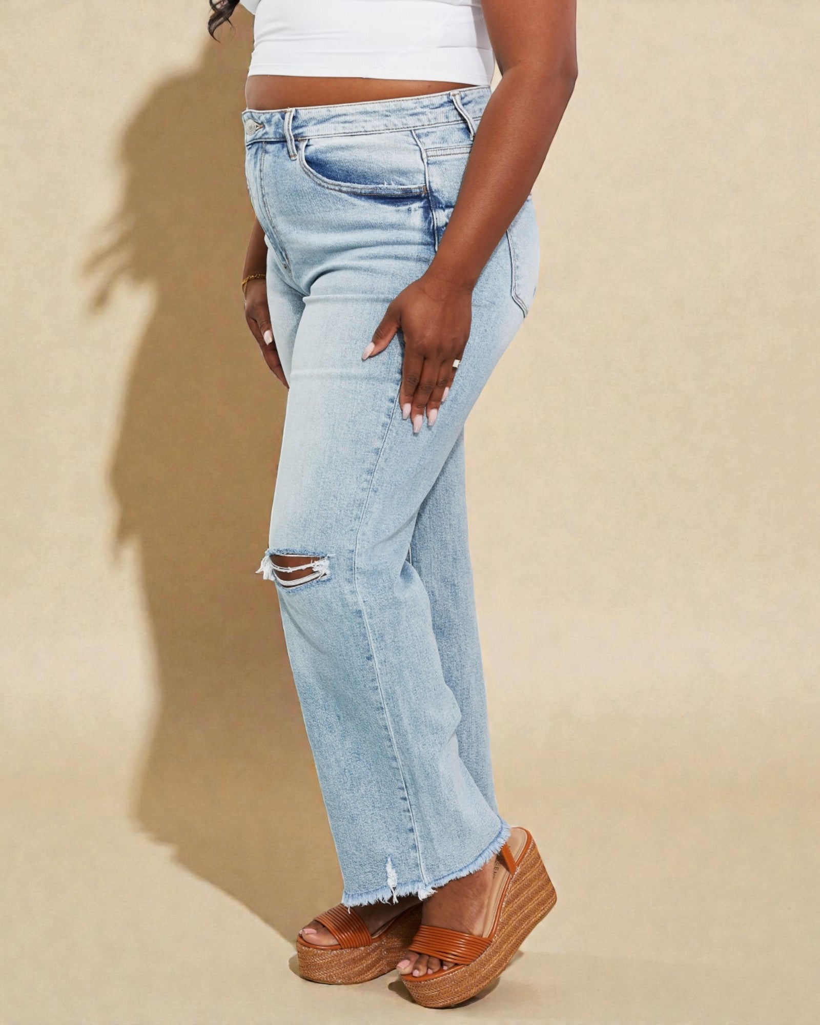 Person wearing light blue distressed jeans on a beige background