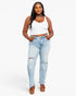 A woman modeling light-wash blue distressed jeans with a white crop top and brown platform sandals against a plain white studio background.
