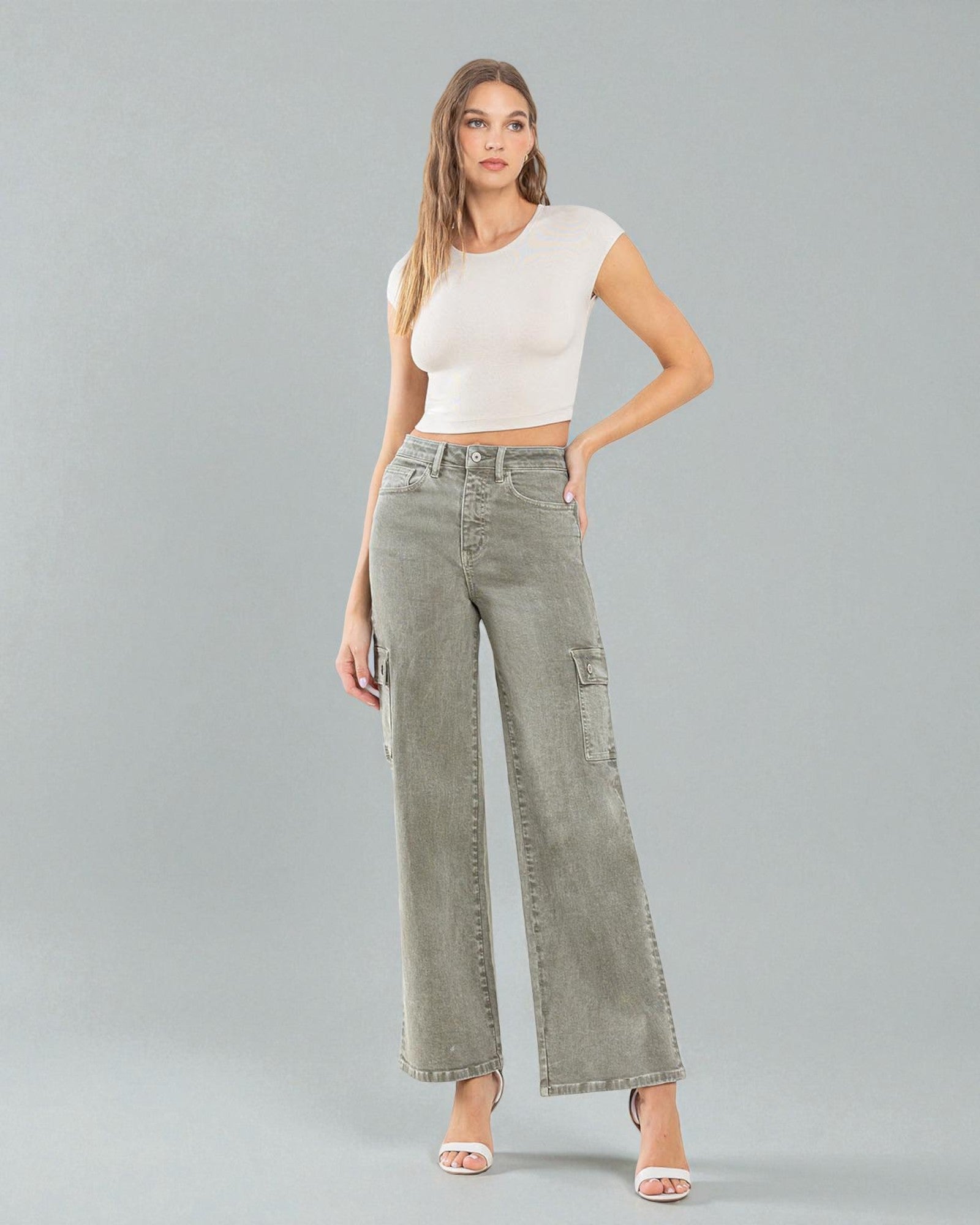 Woman wearing a white crop top and green wide-leg jeans on a gray background