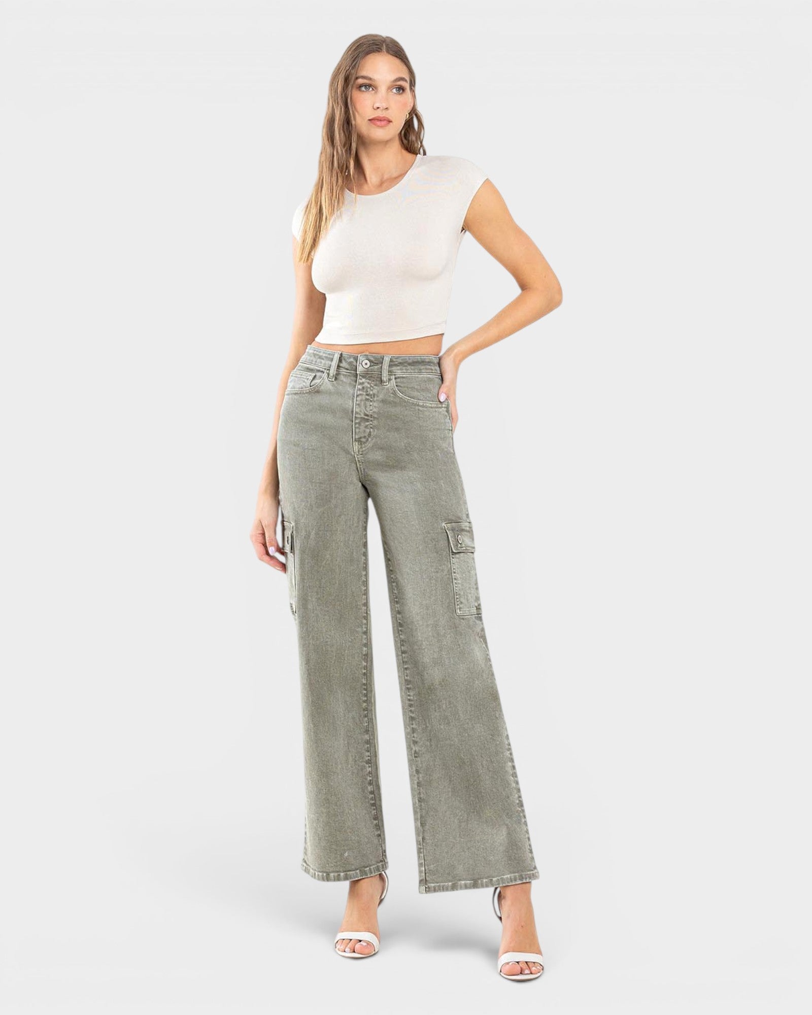 Woman wearing green wide-leg jeans and a white top on a light gray background