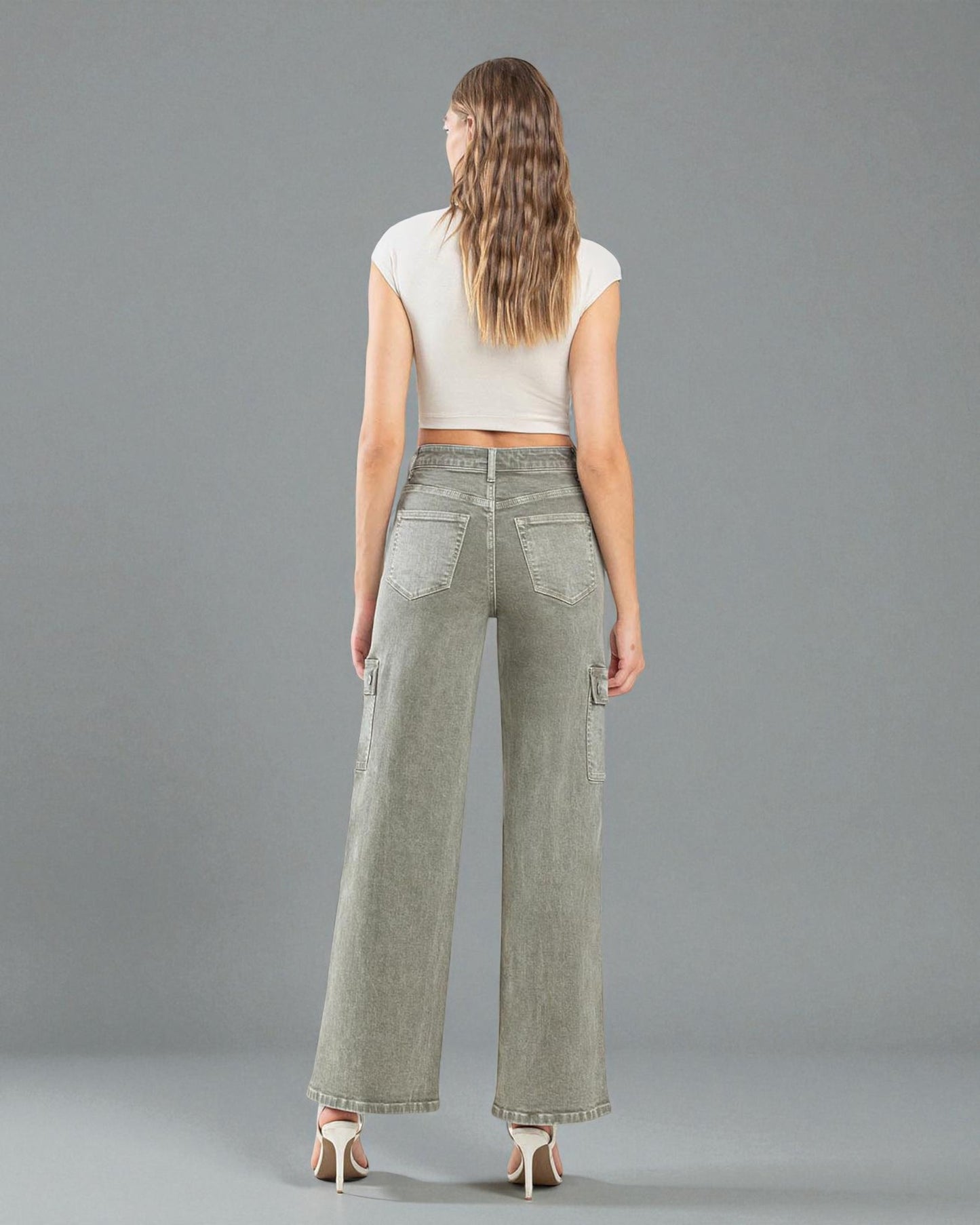 Woman wearing olive green wide-leg pants and a white top on a gray background
