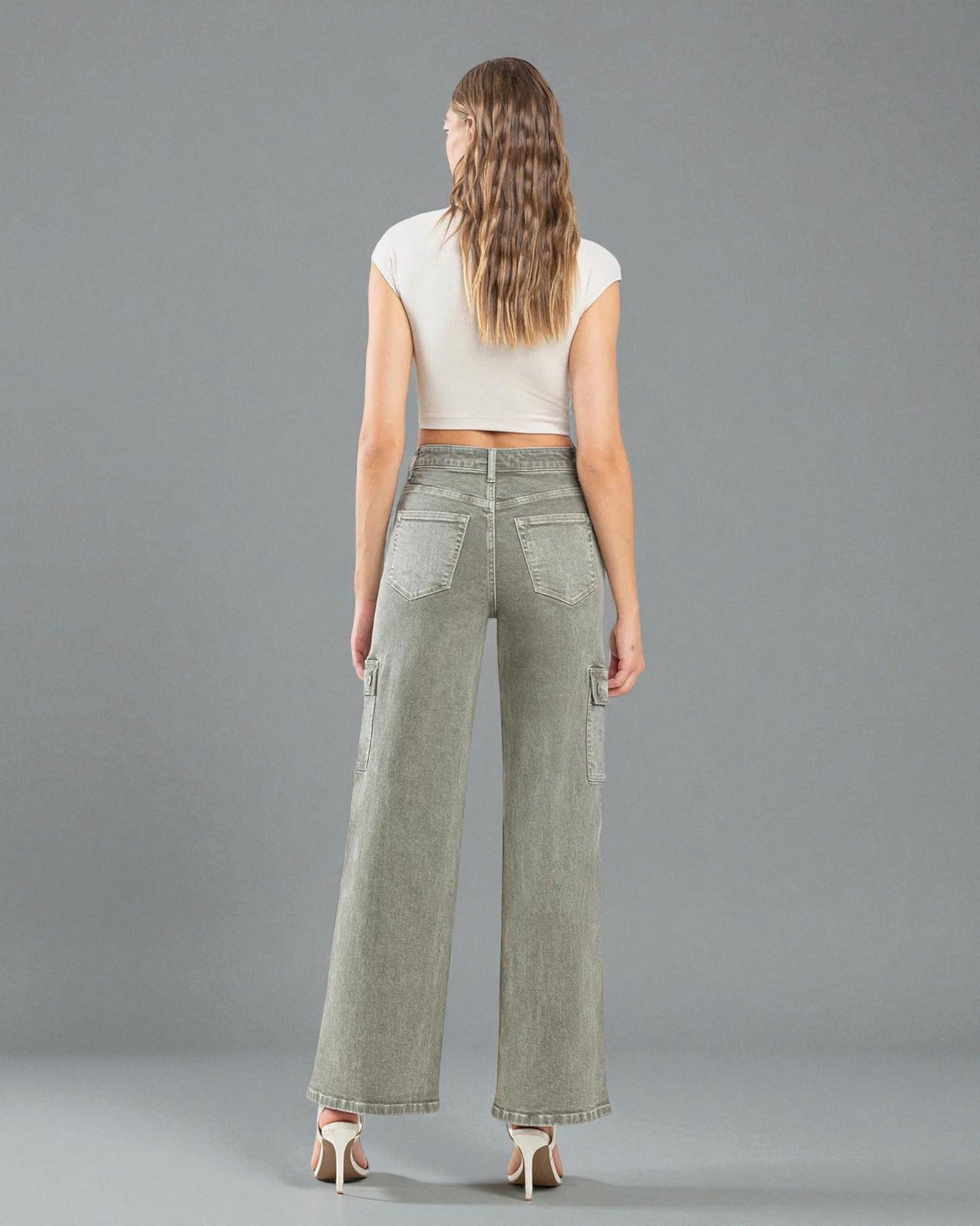 Woman wearing olive green wide-leg pants and a white top on a gray background