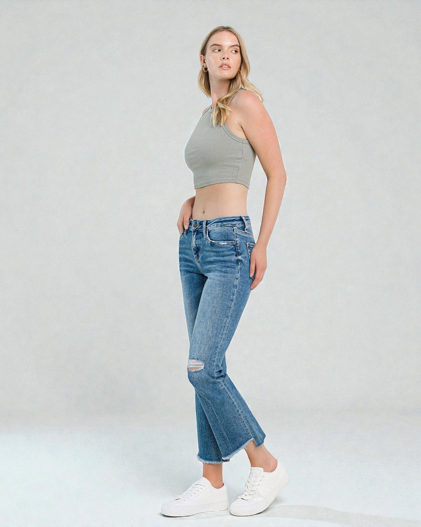 Woman wearing a gray crop top and blue jeans on a white background