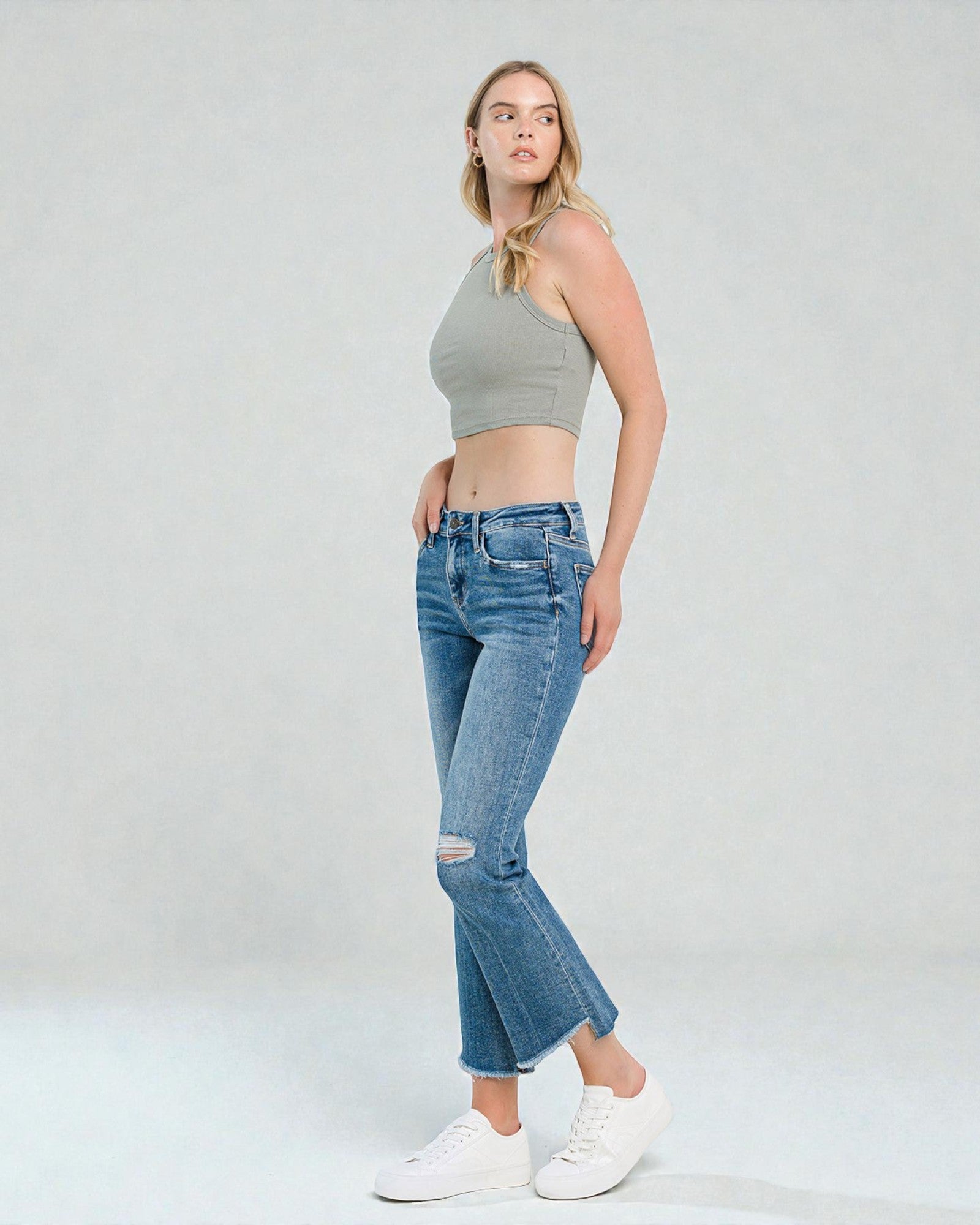 Woman wearing a gray crop top and blue jeans on a white background