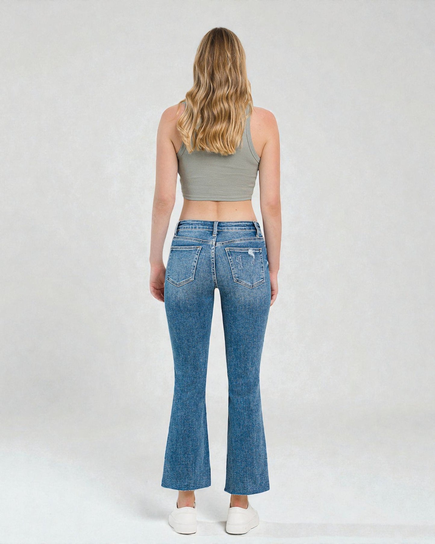 Woman wearing blue jeans and a gray crop top on a white background