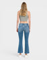 A woman viewed from the back wearing blue flare jeans, a gray crop top, and white sneakers against a light gray studio background.