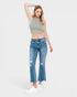 A woman modeling a pair of medium-wash blue cropped flare jeans with distressed details on the thighs and knees, paired with a gray crop top and white sneakers, against a light gray studio background.