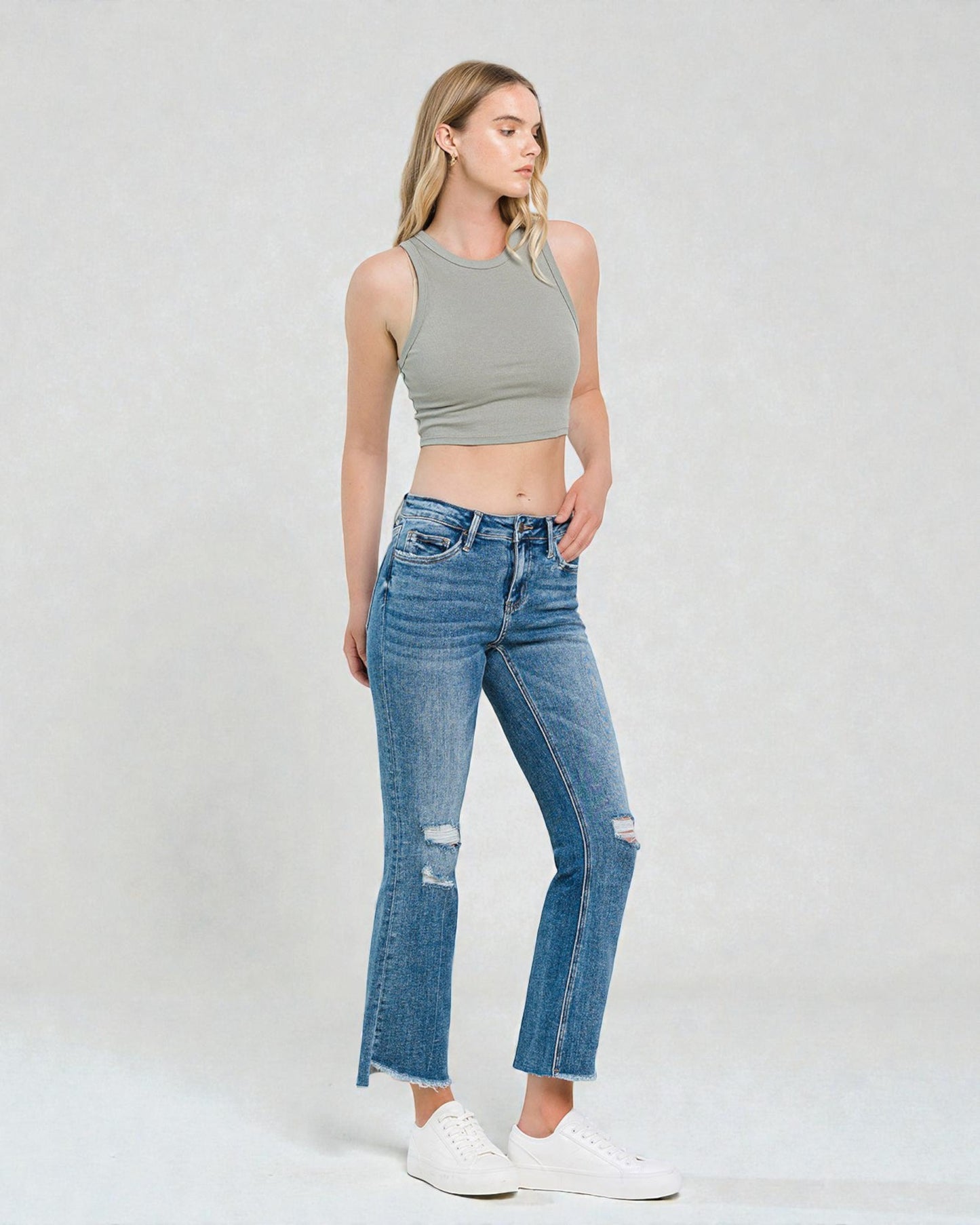 Woman wearing a gray crop top and blue jeans on a white background