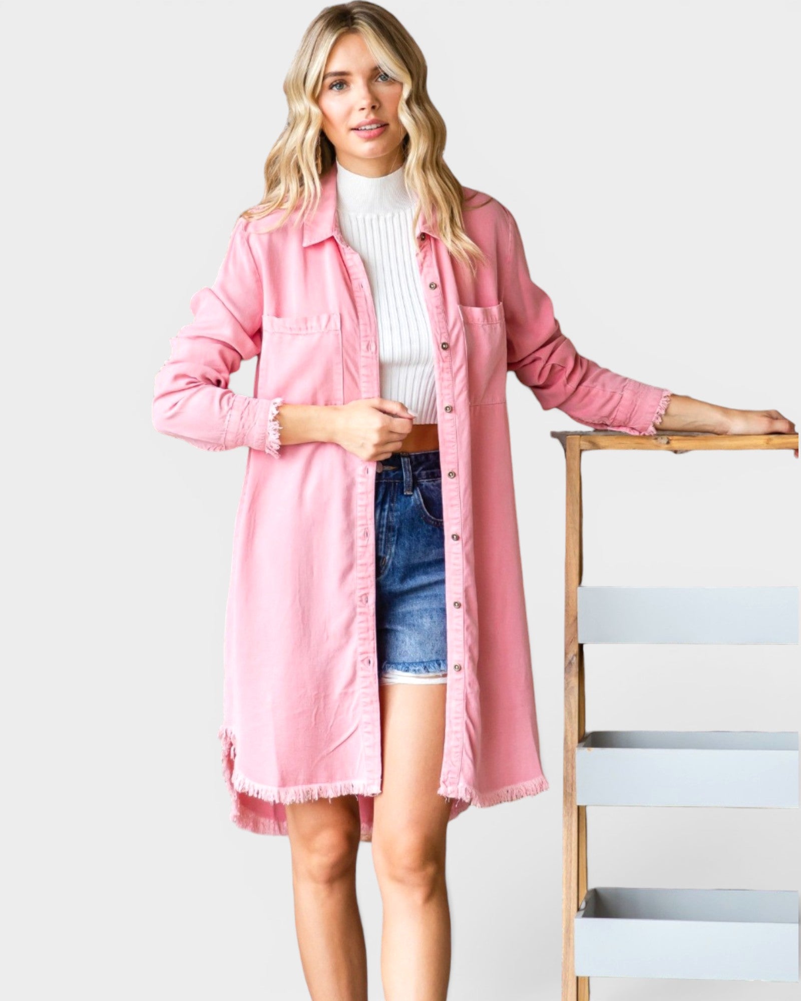 Woman wearing a pink coat over a white sweater and denim shorts on a white background