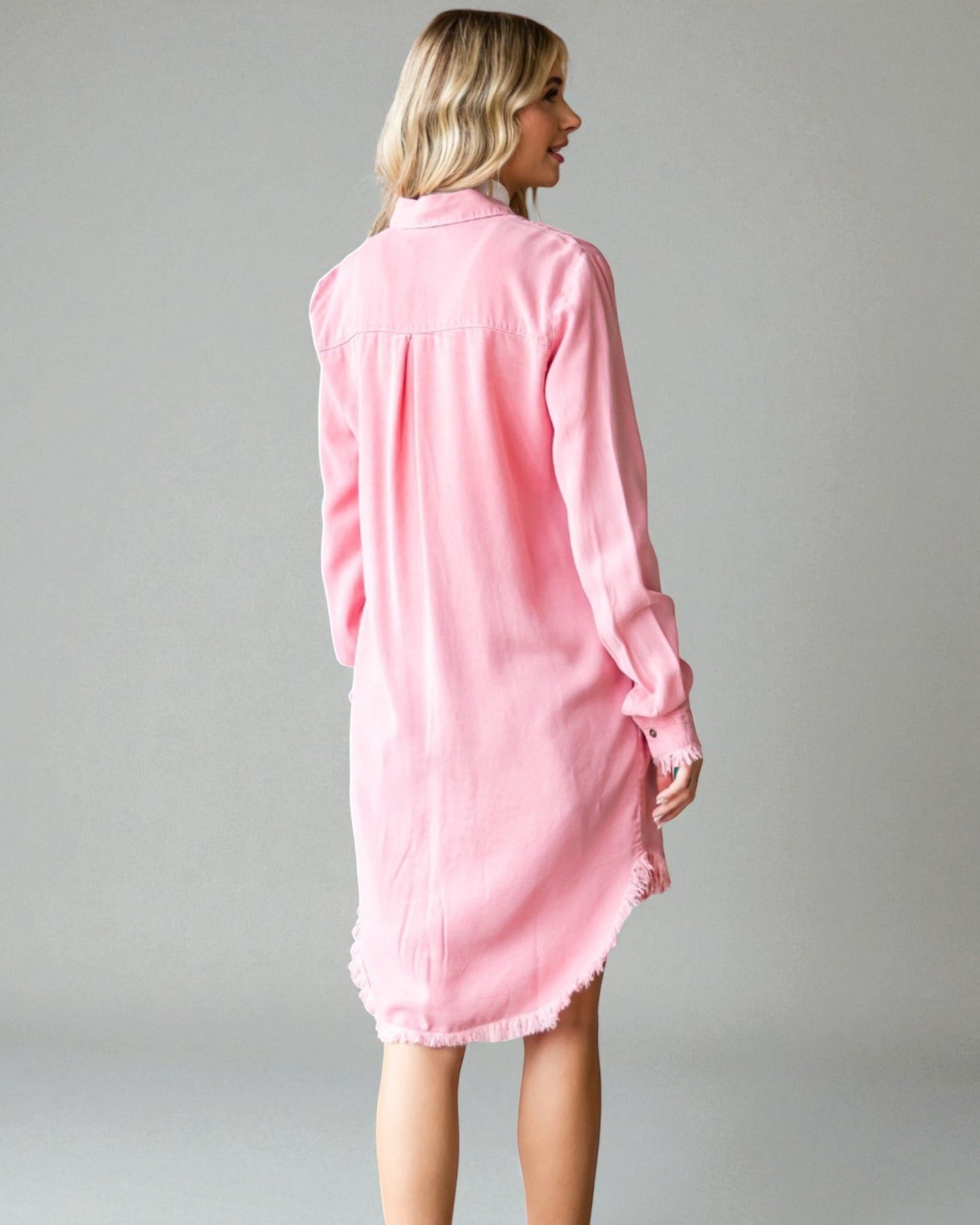 Woman wearing a pink shirt dress against a gray background