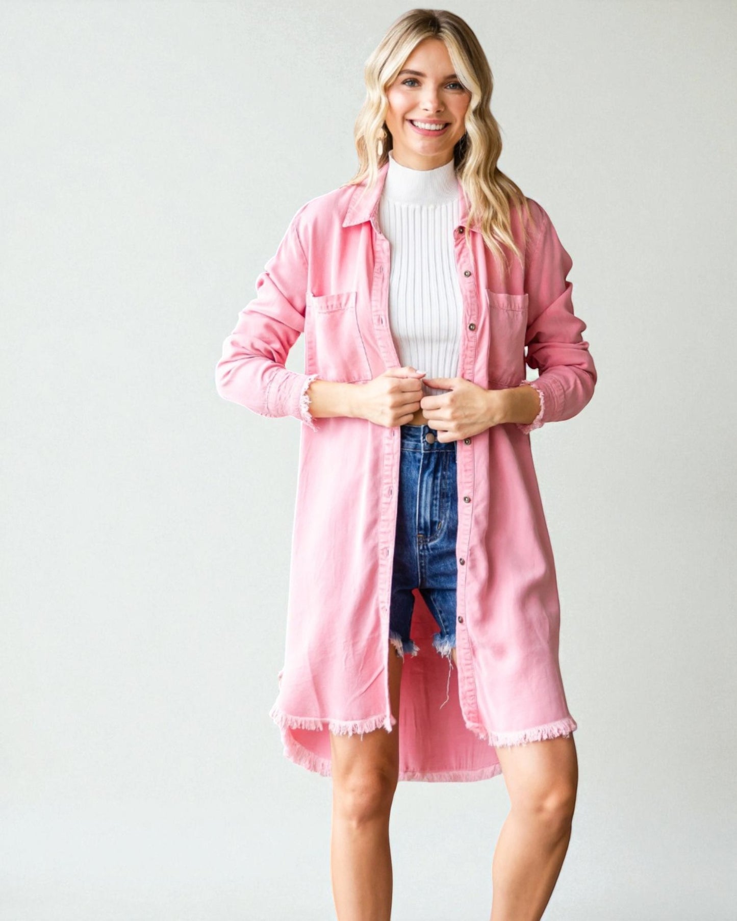 Woman wearing a pink shirt over a white turtleneck and blue jeans on a plain background