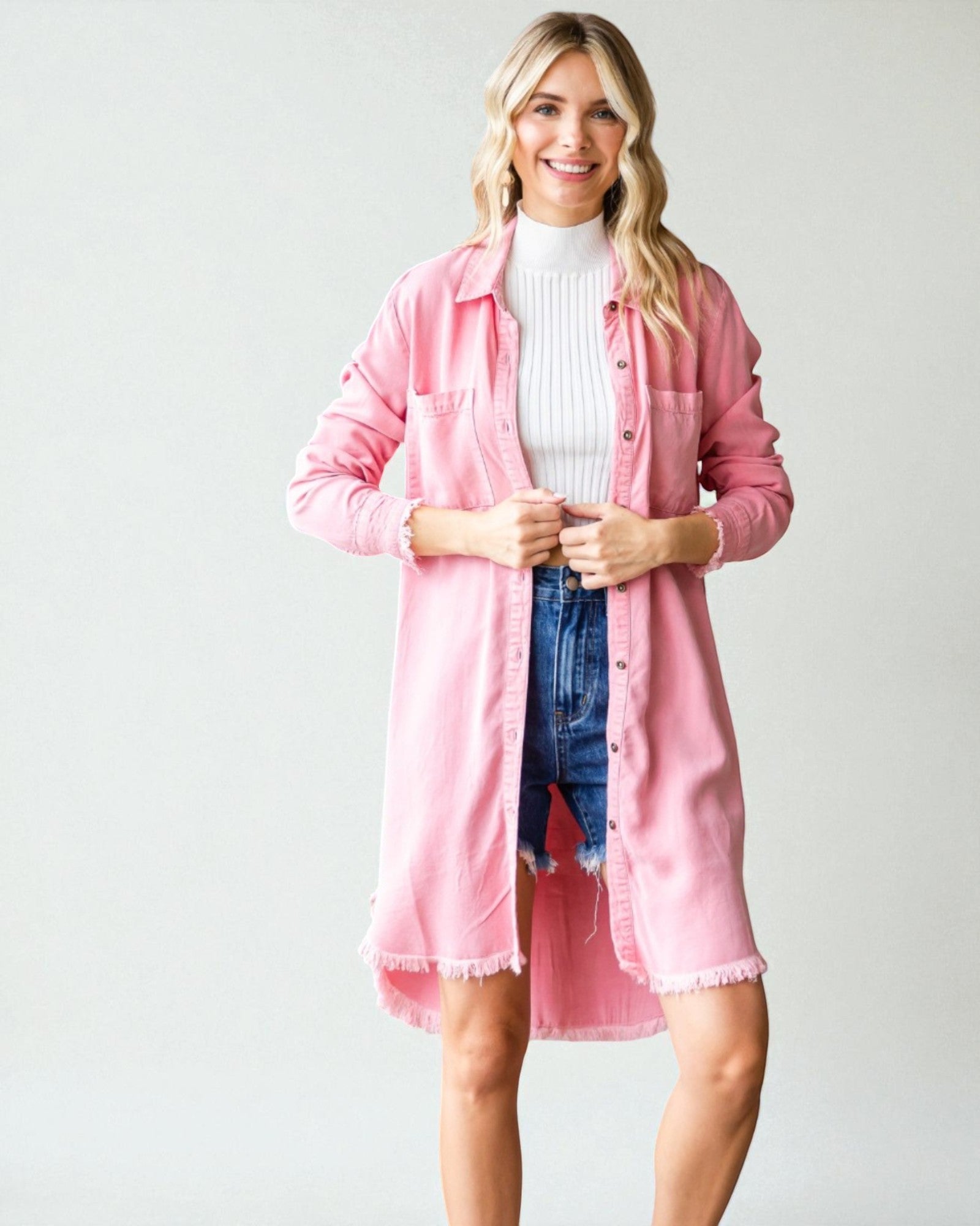 Woman wearing a pink shirt over a white turtleneck and blue jeans on a plain background