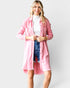 Woman wearing a pink cardigan over a white sweater and blue jeans on a plain background