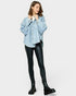 Woman wearing a blue patterned shirt, black leather pants, and black boots on a white background