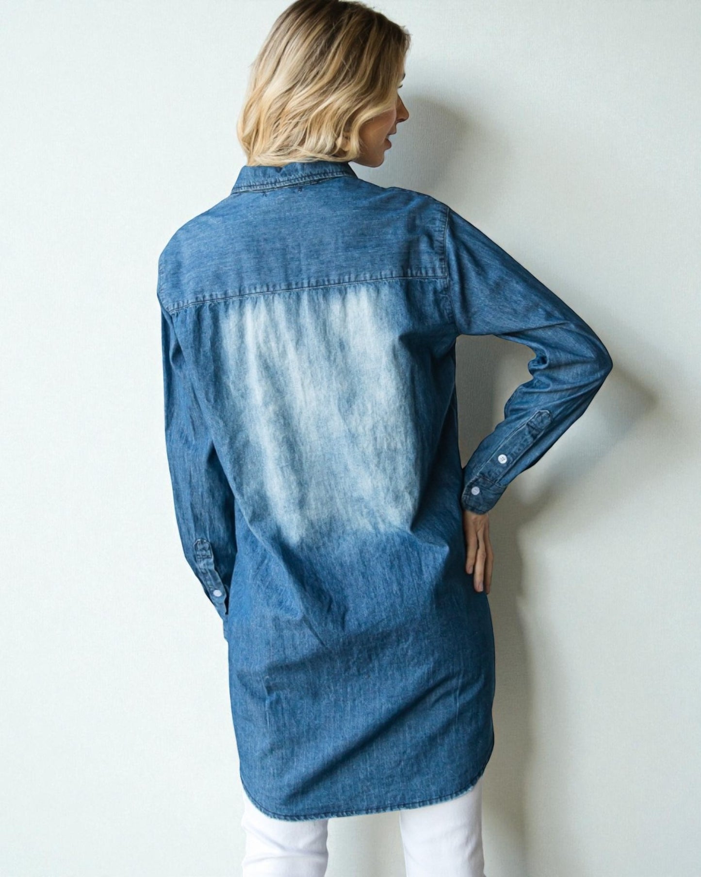 Person wearing a blue denim shirt against a white wall