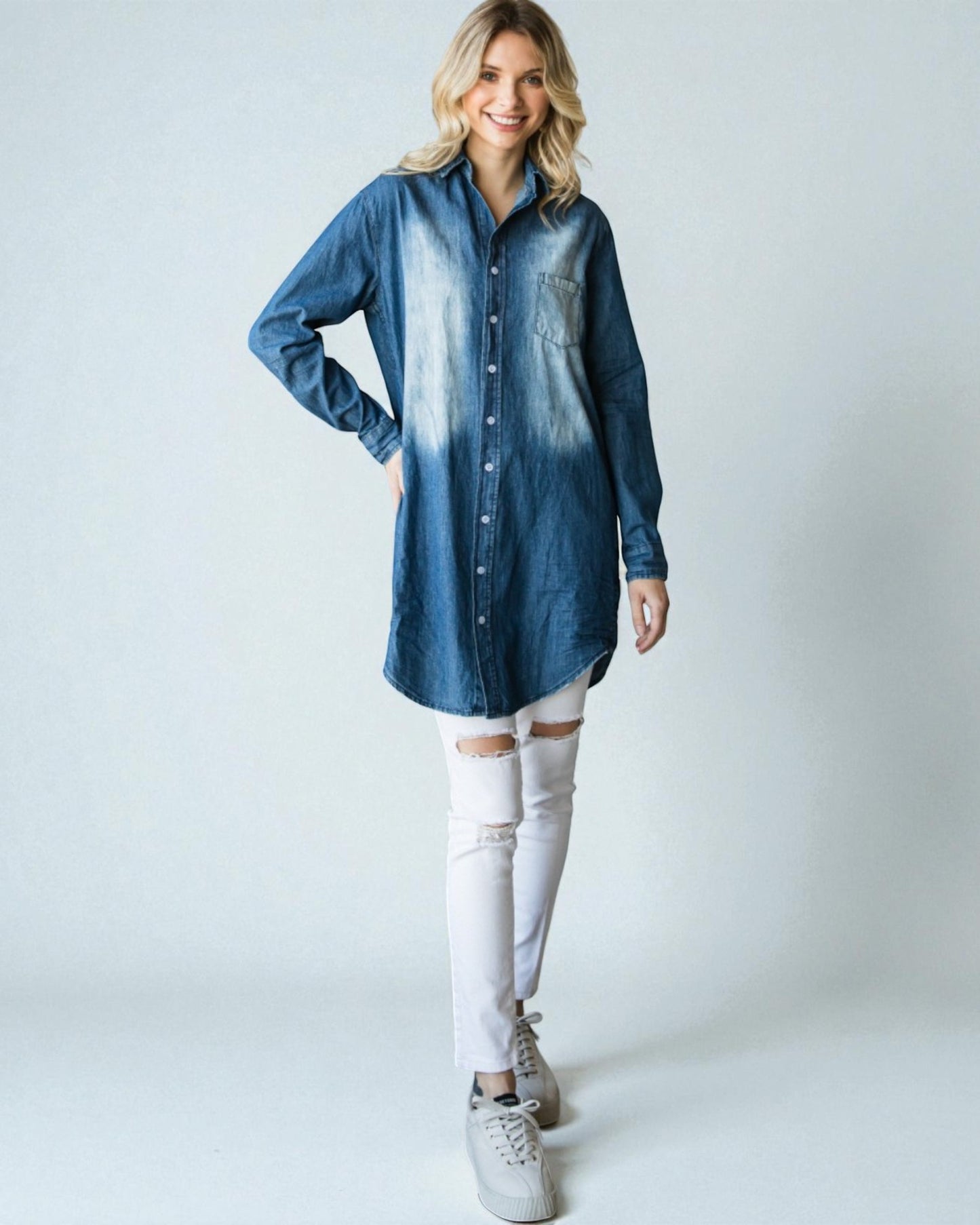 Woman wearing a blue denim shirt and white pants on a plain background