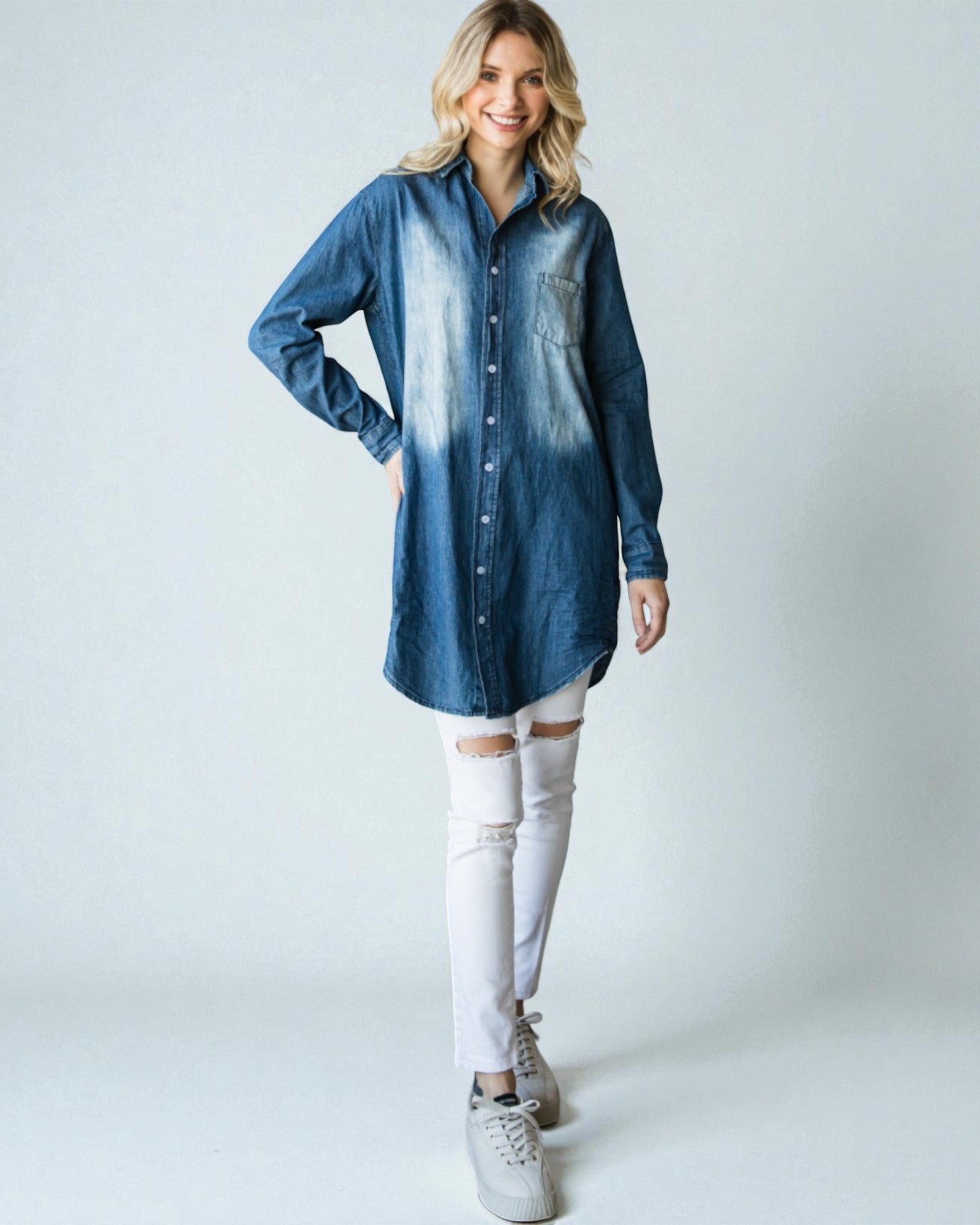 Woman wearing a blue denim shirt and white pants on a plain background