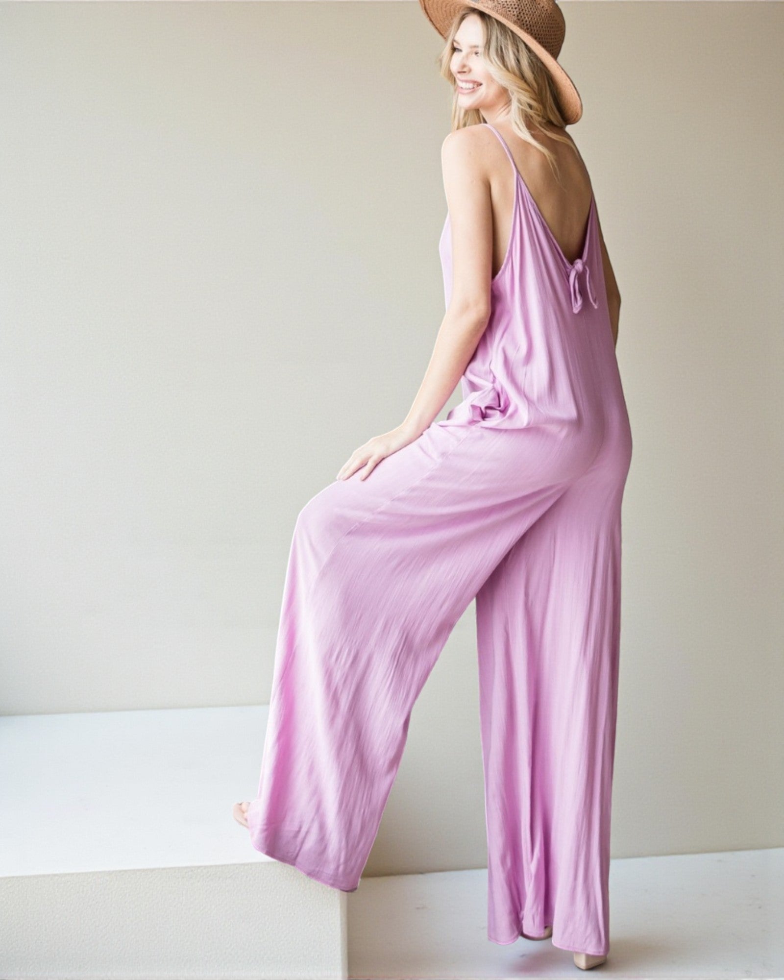 Woman wearing a pink jumpsuit sitting on a white surface with a plain background