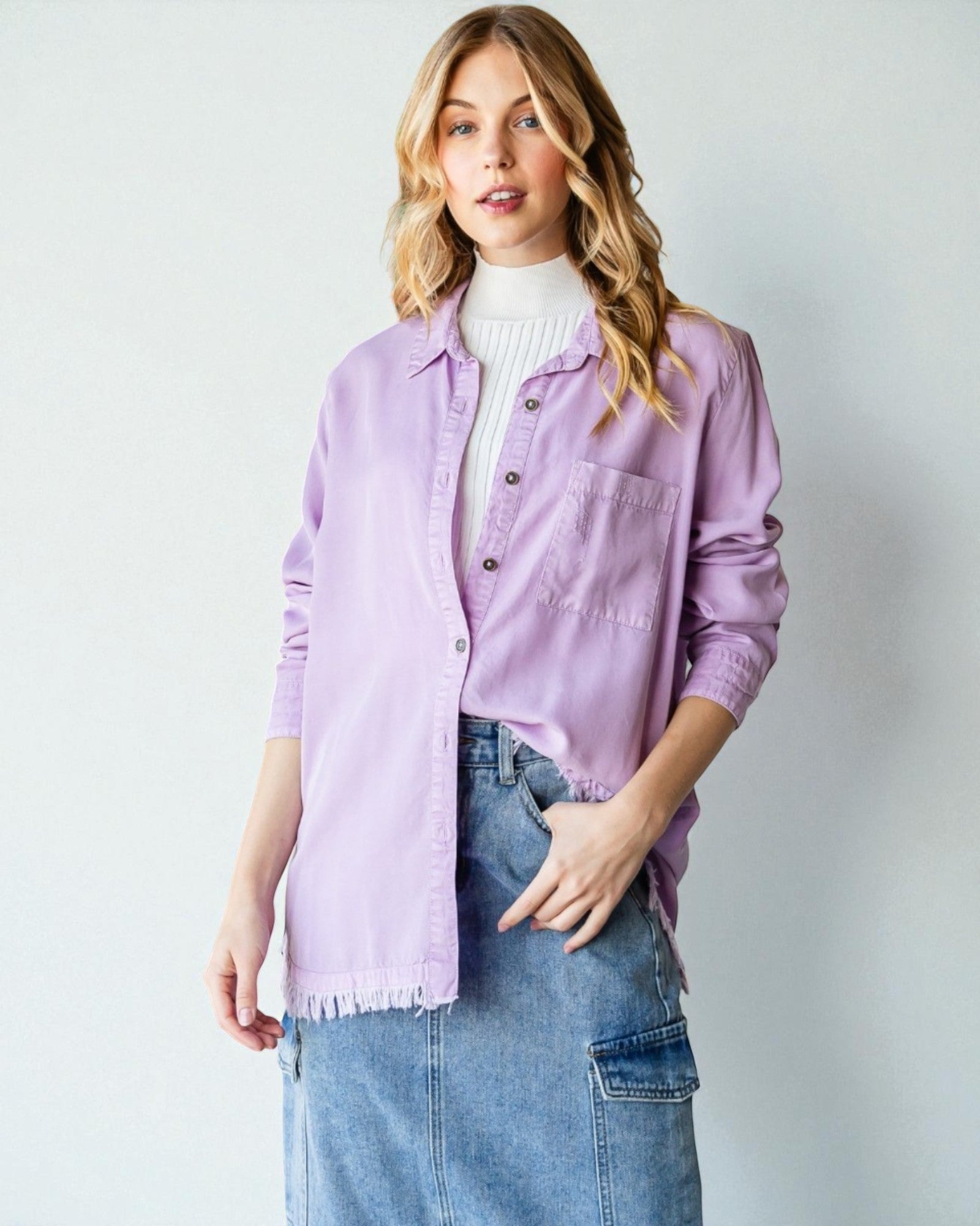 Woman wearing a light purple jacket over a white sweater and blue jeans on a plain background