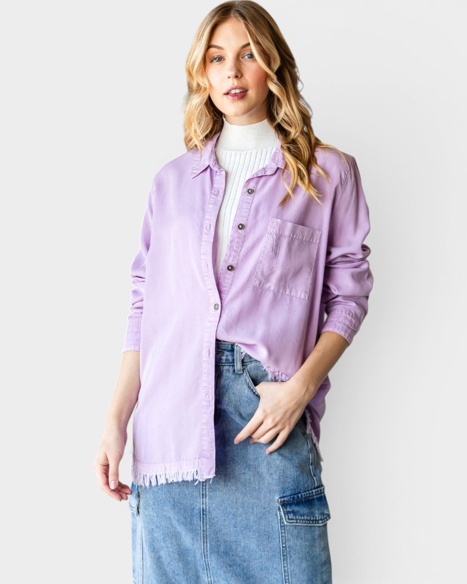 Woman wearing a light purple denim jacket over a white turtleneck and blue jeans on a plain background