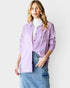 Woman wearing a light purple denim jacket over a white turtleneck and blue jeans on a plain background