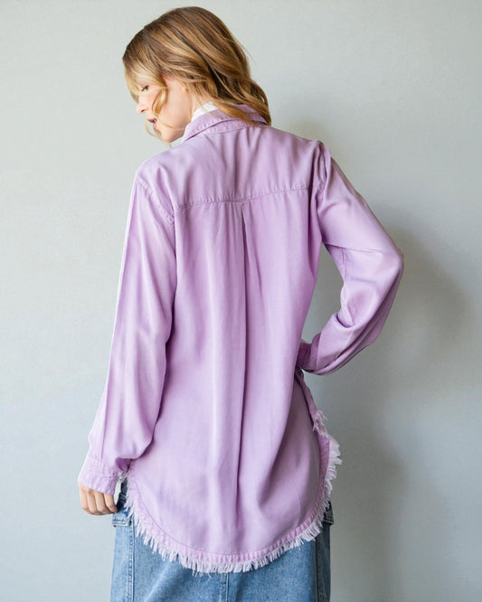 Person wearing a light purple shirt with frayed hem against a plain background