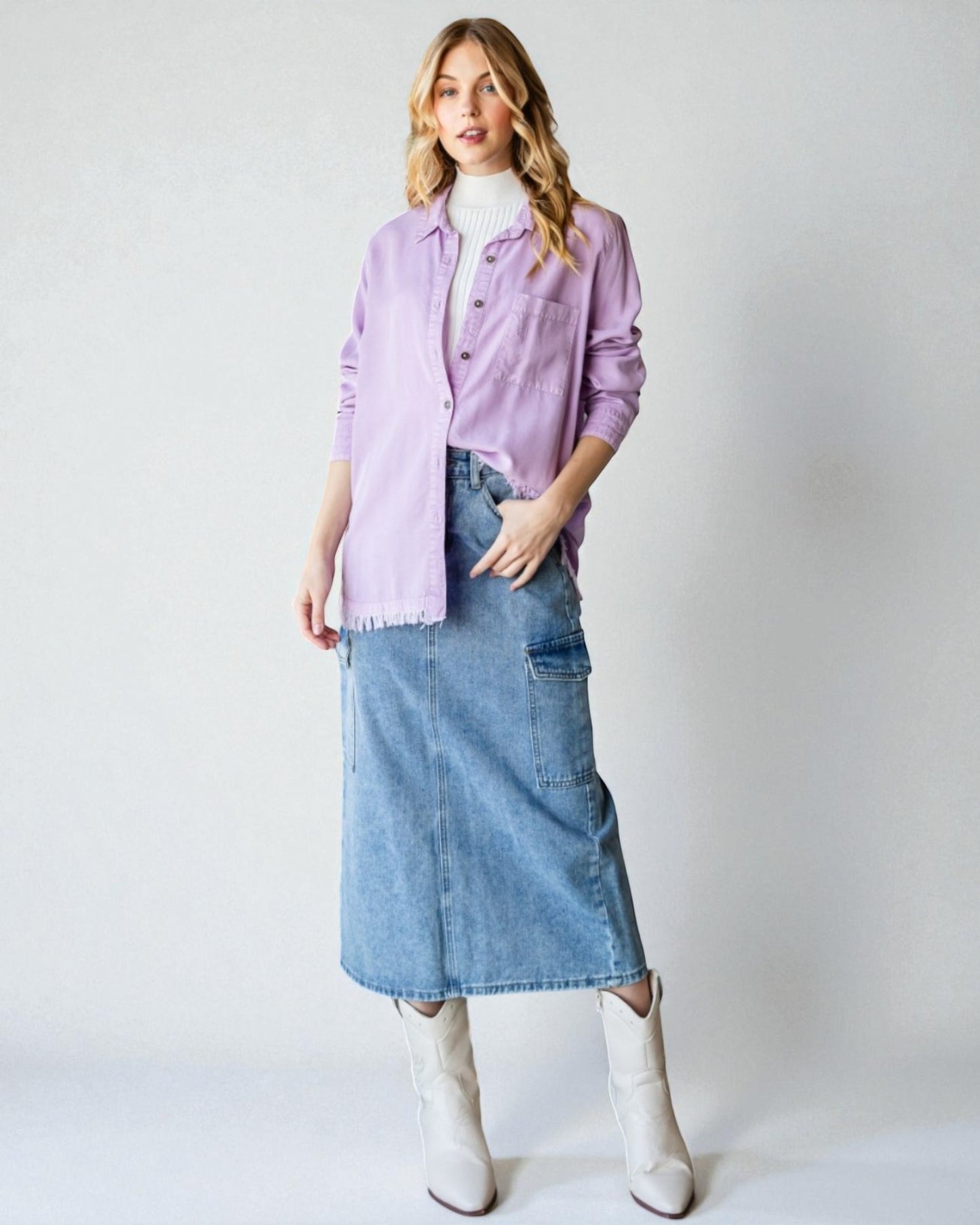 Woman wearing a light purple shirt, blue denim skirt, and white boots on a plain background