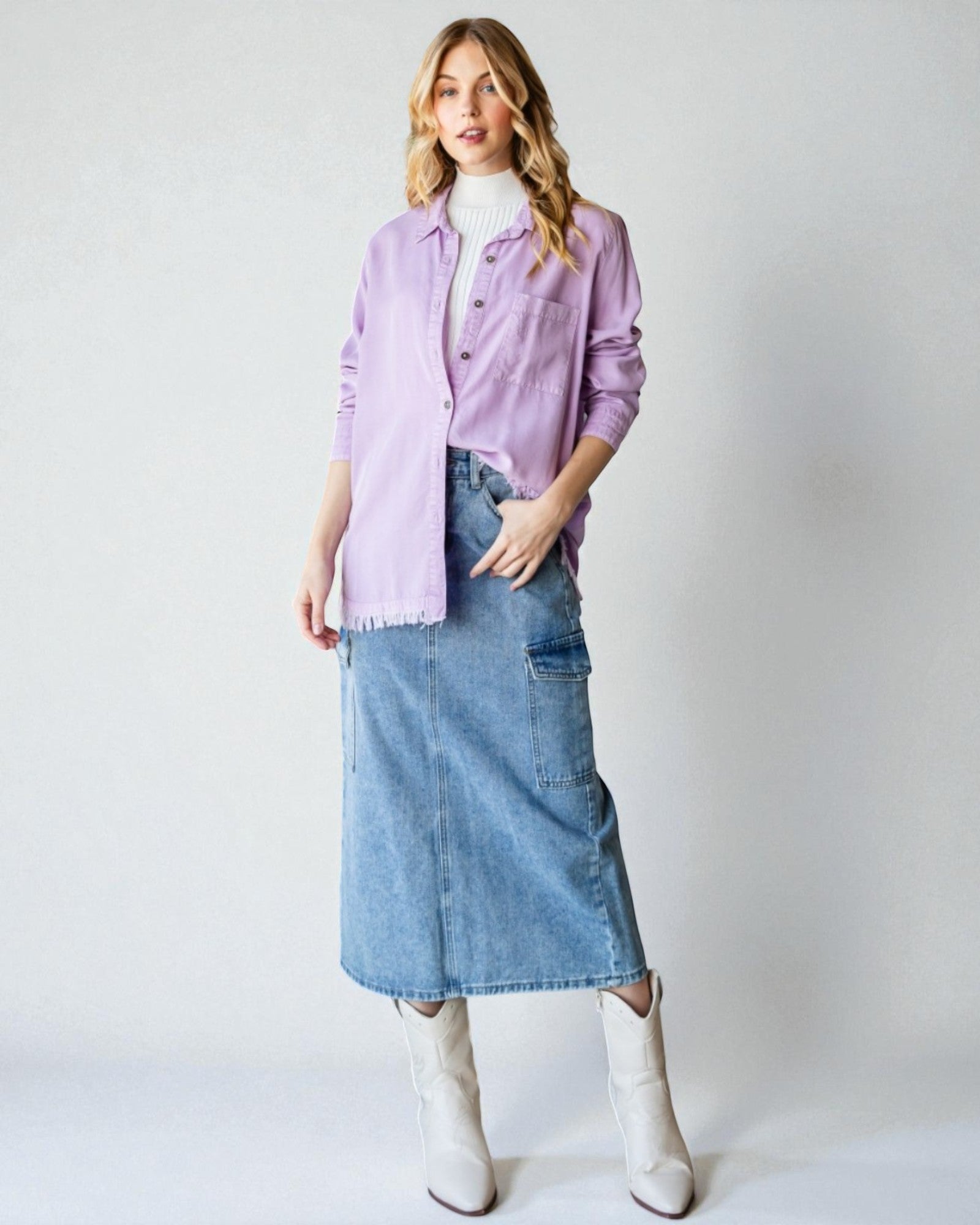 Woman wearing a light purple shirt, blue denim skirt, and white boots on a plain background