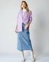 Woman wearing a light purple shirt, blue denim skirt, and white boots on a plain background