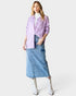 Woman wearing a light purple shirt, denim skirt, and white boots on a white background