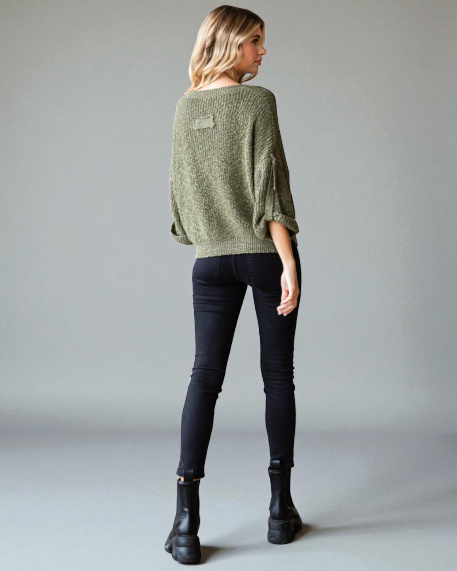 Person wearing a green sweater and black pants on a plain background