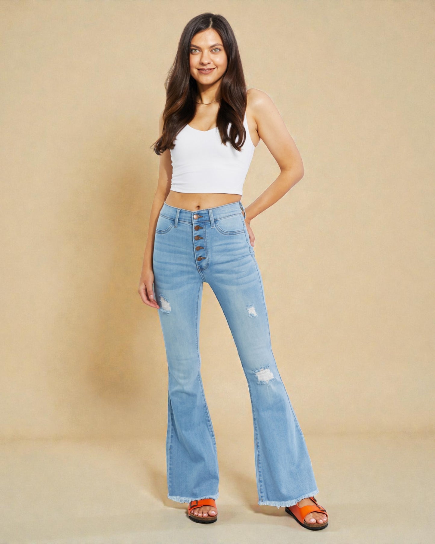Woman wearing a white crop top and light blue flared jeans on a beige background