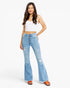 A woman modeling light-wash blue flare jeans with a button fly, paired with a white crop top and orange sandals, against a plain white studio background.