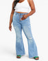 A model wearing light-wash blue distressed flare jeans with a button fly, styled with a white crop top and green sandals against a plain white background.