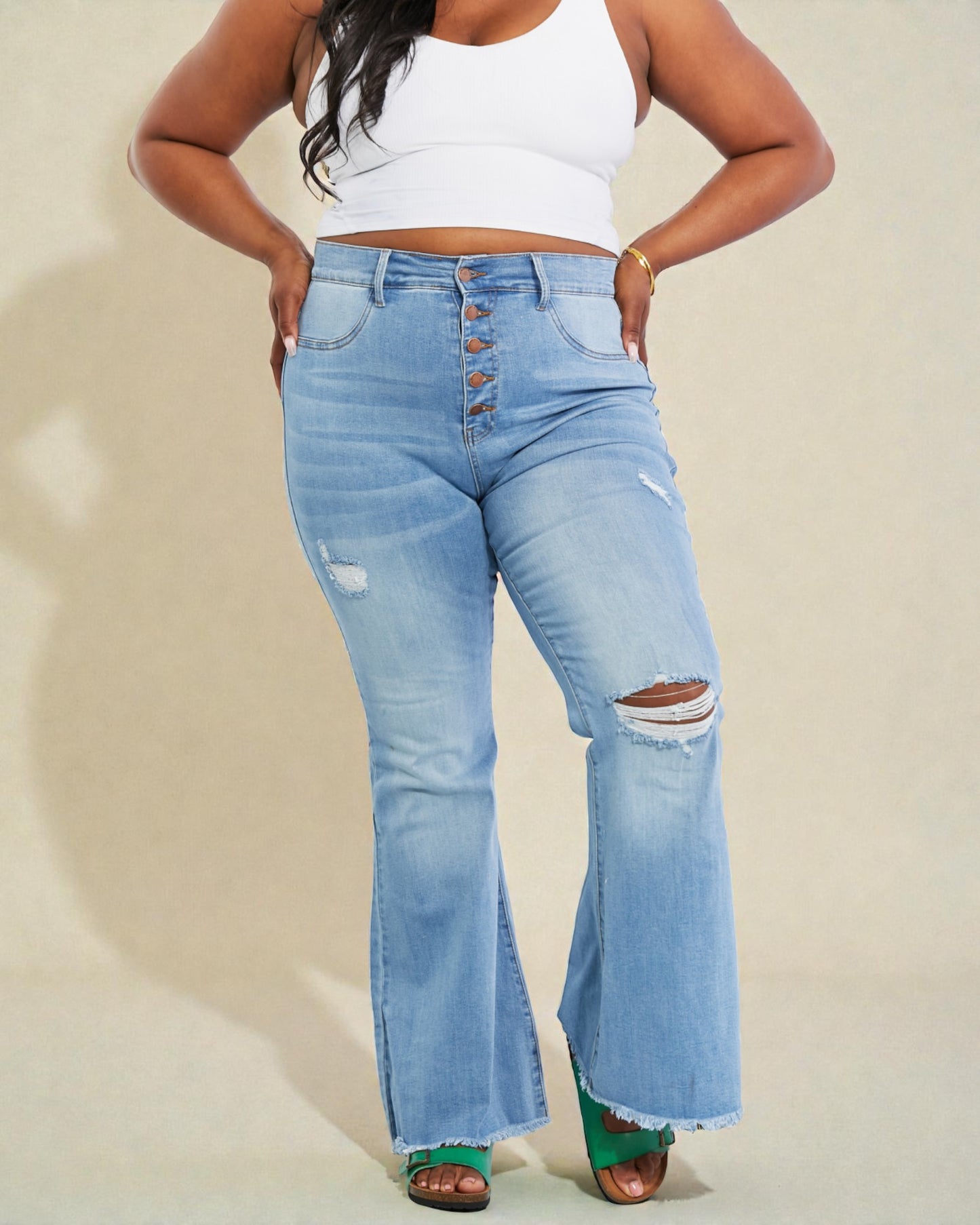 Person wearing light blue distressed jeans and a white crop top on a beige background