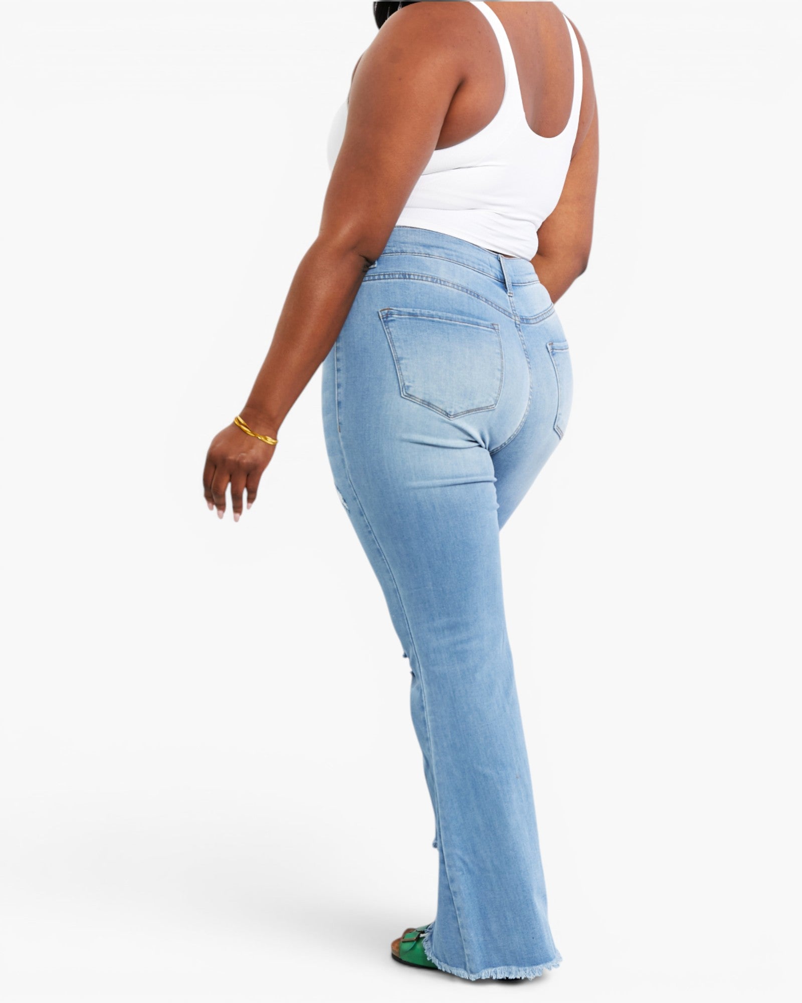 A model shown from the back wearing light-wash blue flare jeans and a white tank top, standing against a plain white studio background.