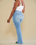 Person wearing light blue jeans and a white tank top on a beige background