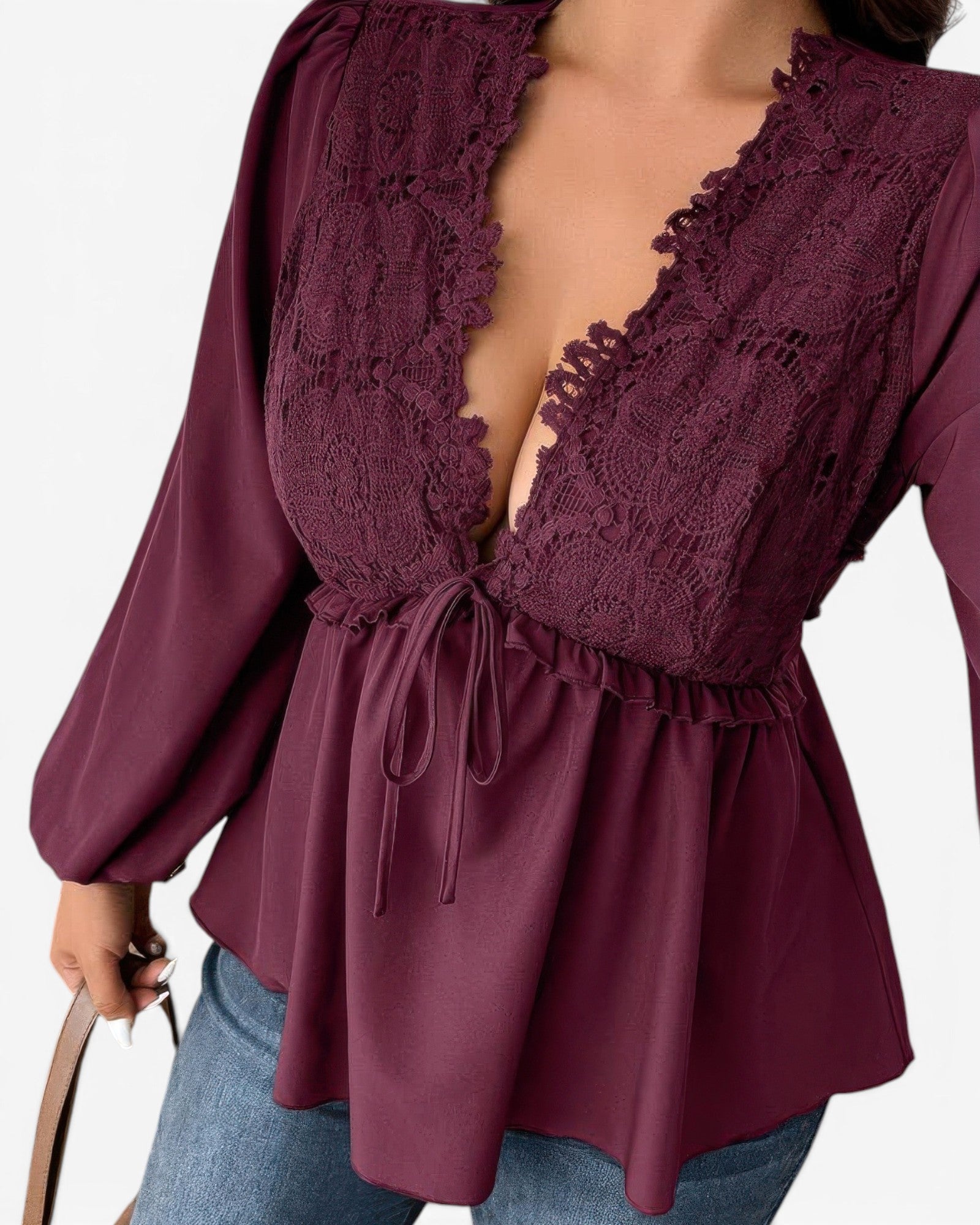 A close-up of a woman wearing a deep burgundy long-sleeve blouse with a lace-trimmed plunging neckline and a drawstring waist, paired with blue jeans against a plain white background.