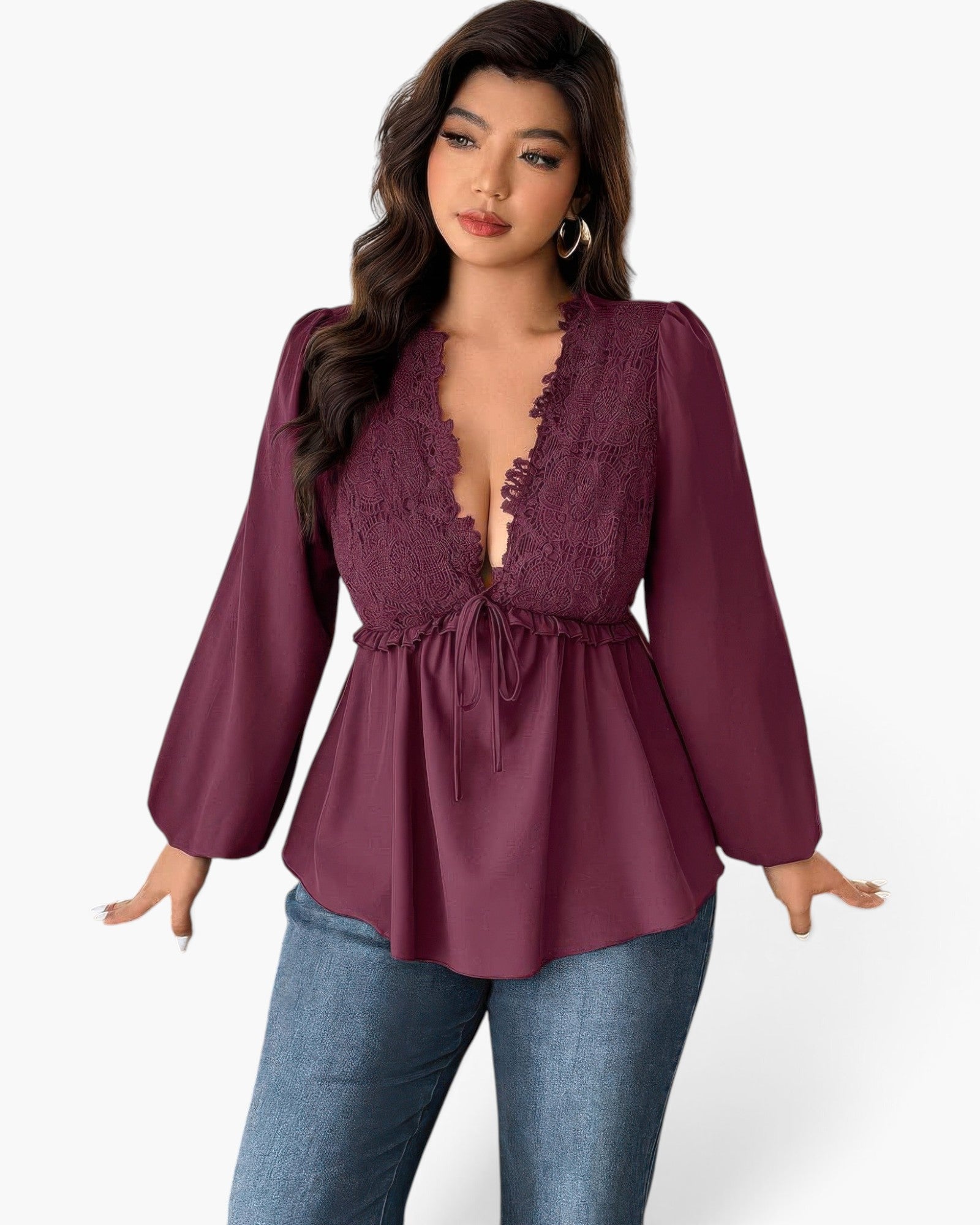 A woman modeling a long-sleeve deep plum purple top with a lace V-neckline and drawstring waist, paired with blue jeans against a light gray background.