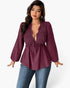 A woman modeling a long-sleeve deep plum purple top with a lace V-neckline and drawstring waist, paired with blue jeans against a light gray background.