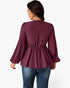A woman shown from the back wearing a long-sleeve peplum blouse in a deep burgundy or plum color, paired with blue jeans, against a plain light gray studio background.