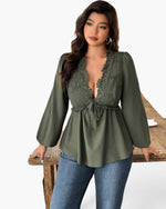 A woman models an olive green long-sleeve blouse with a lace V-neck bodice and drawstring waist, paired with blue jeans, standing behind a rustic wooden table against a white studio background.
