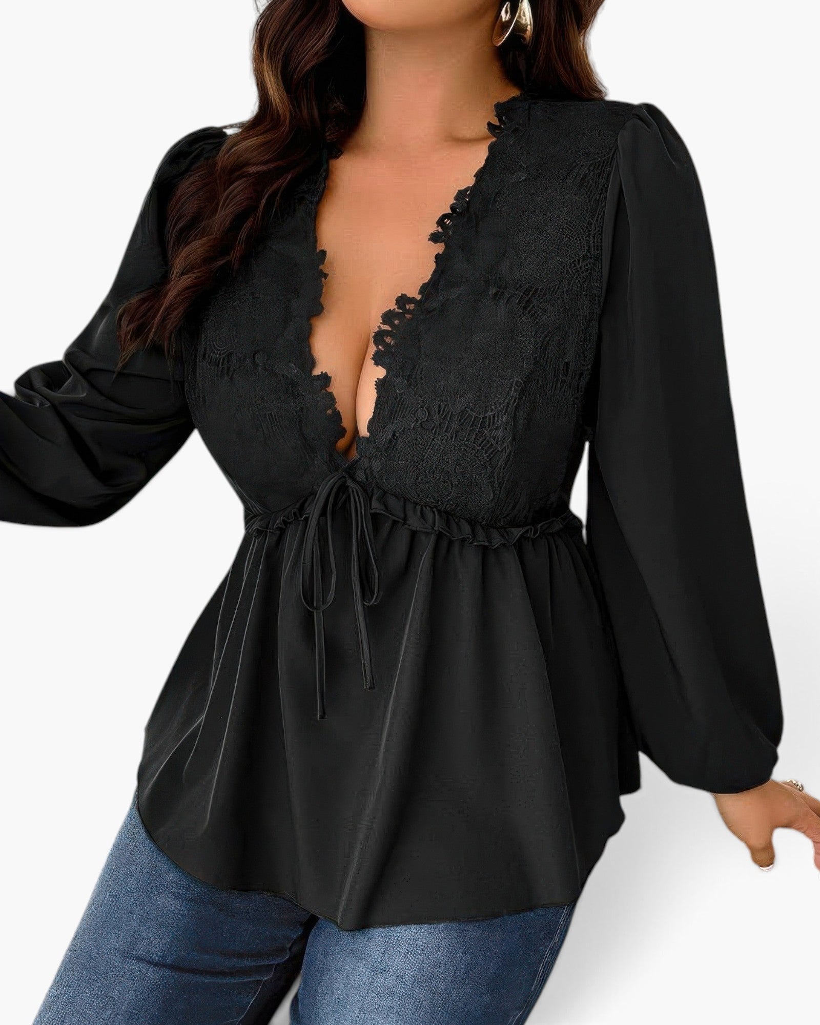 A woman wearing a black long-sleeve blouse with a deep V-neckline, lace-like ruffle trim, and a drawstring waist, paired with blue jeans against a plain light background.