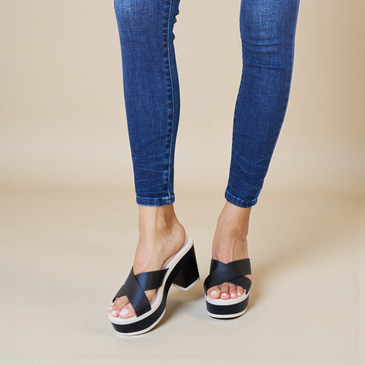 Black platform sandals worn with blue jeans on a beige background