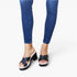 A person wearing blue skinny jeans and black platform slide sandals with crisscross straps, shown from the calves down on a clean white studio background.