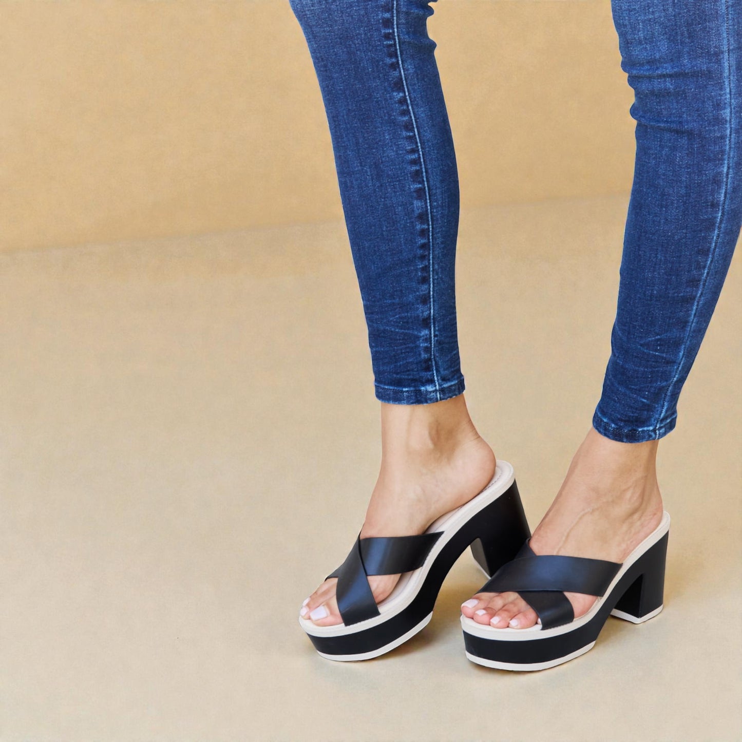 Black platform sandals worn with blue jeans on a beige background