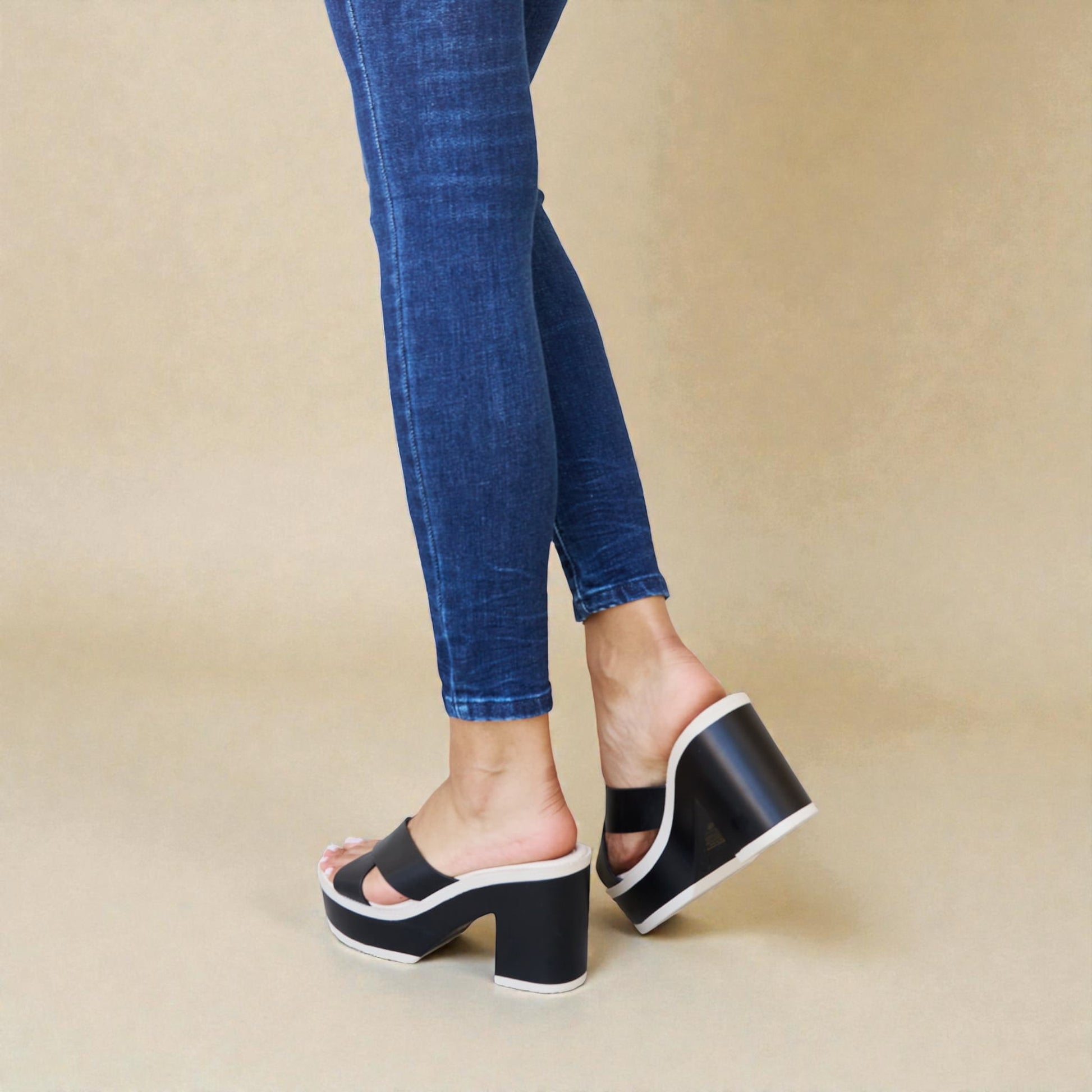 Person wearing blue jeans and black platform sandals on a beige background