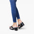 A person wearing blue skinny jeans and black platform mule sandals with white trim, shown from the calves down against a clean white studio background.