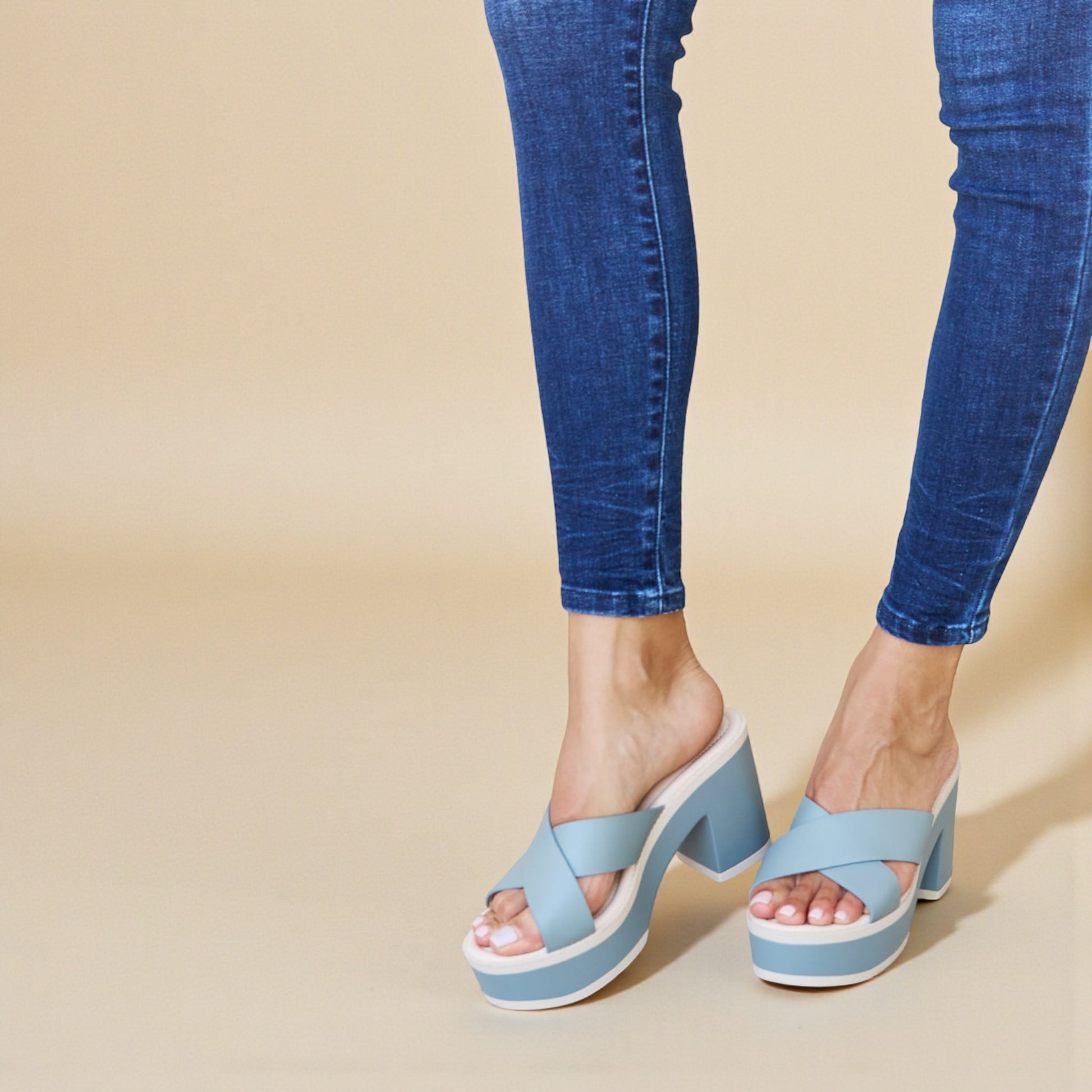 Blue sandals worn with blue jeans on a beige background
